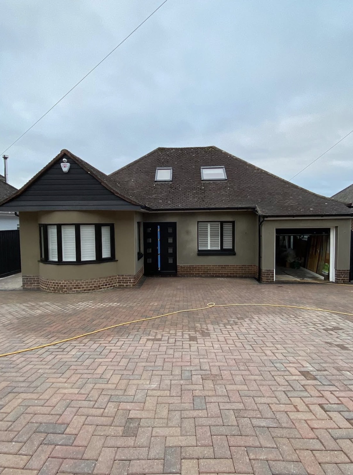 Brown K Rend silicone render finish on a detached bungalow with black cladding and brick plinth